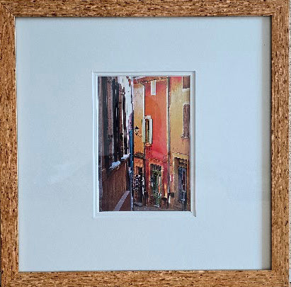 Framed artwork of a colorful street scene with a light blue mat