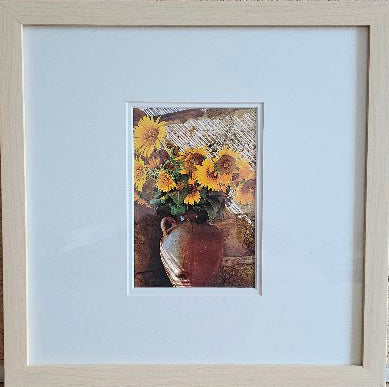 Framed artwork of sunflowers in a vase with a light blue mat.