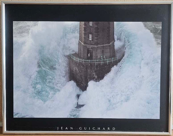 Framed artwork of a lighthouse surrounded by large waves, signed 'Jean Guichard'.